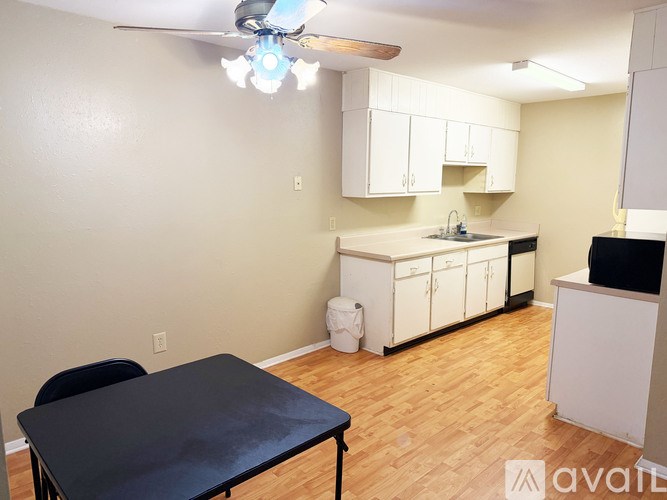 A kitchen with a table and chairs in the foreground and a ceiling fan with lights.