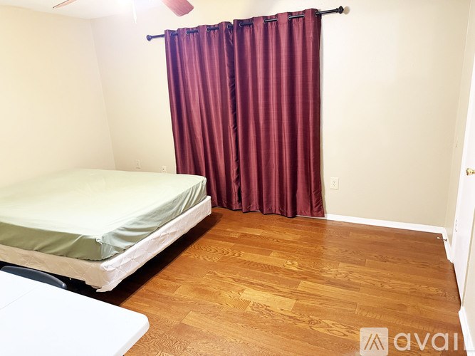 A bedroom with a bed, wooden floor, and a red curtain.