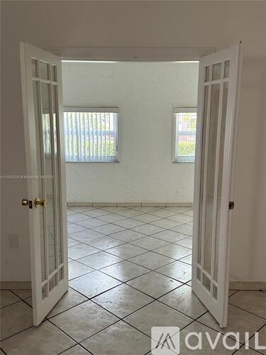 A room with white walls and a tiled floor is shown through an open door.