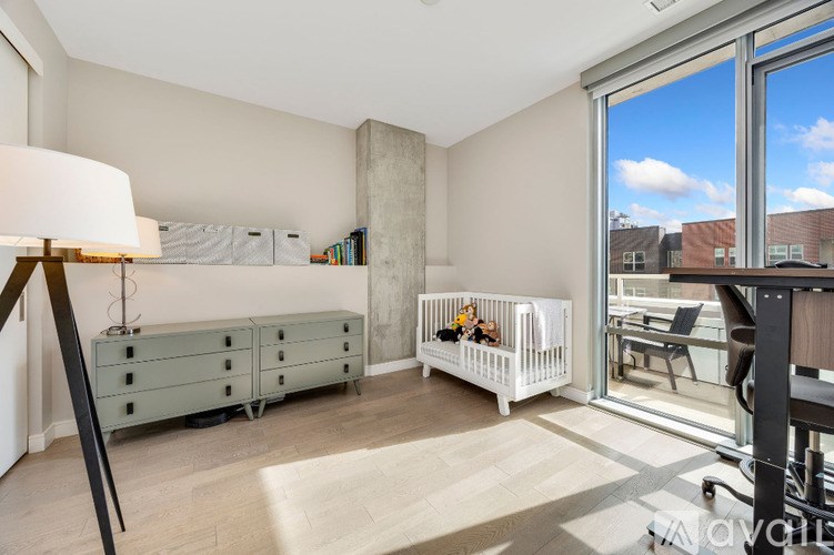 A baby is sitting in a white crib in a room with a large window.