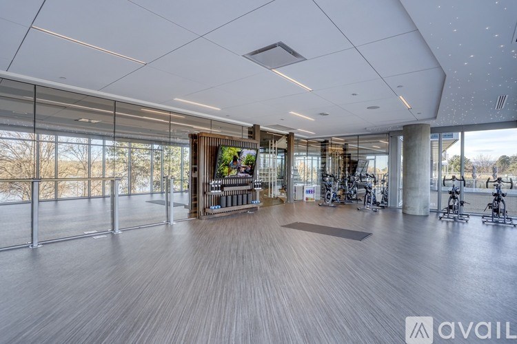 A spacious room with wooden floors and a large window overlooking a tree-lined street.