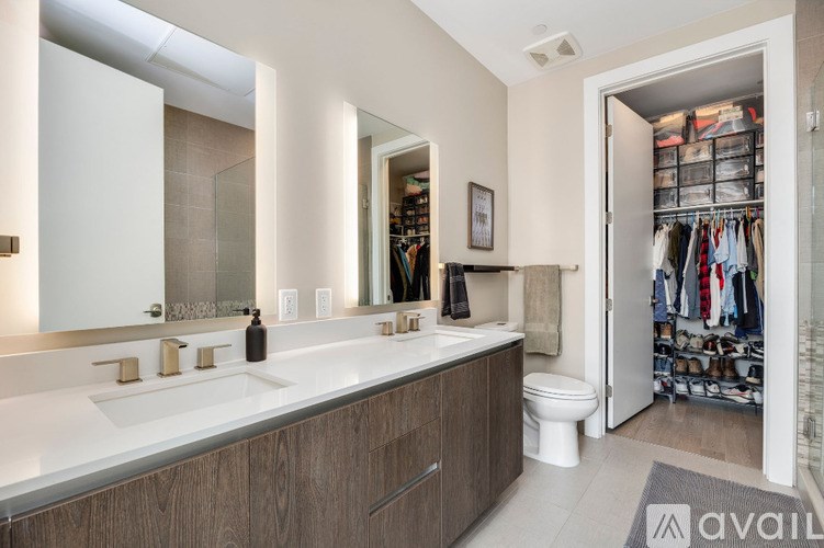 A bathroom with a white counter top and a walk in closet.