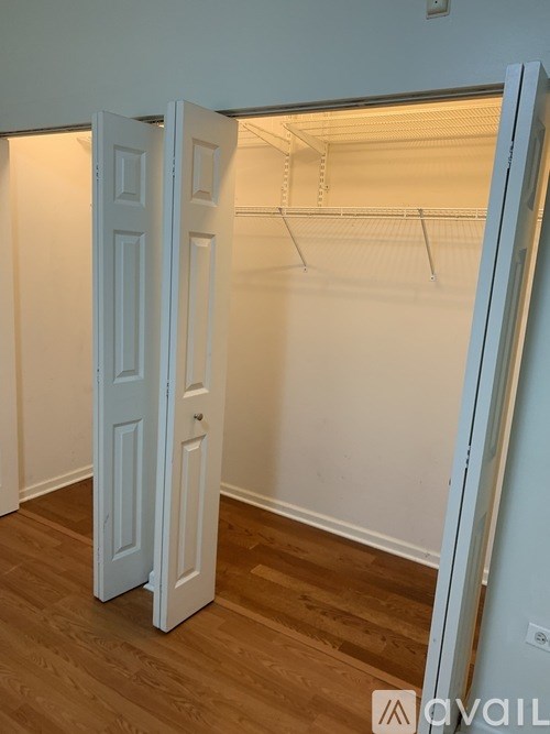 A white door is open to reveal a small, empty, white closet with a wooden floor.