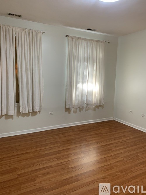 A room with wooden flooring and two windows with curtains.