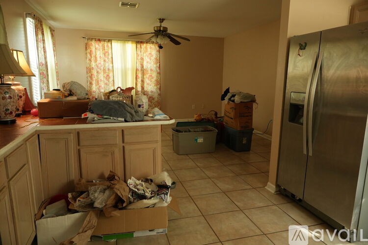 A kitchen with a refrigerator, a box of clothes and a fan.