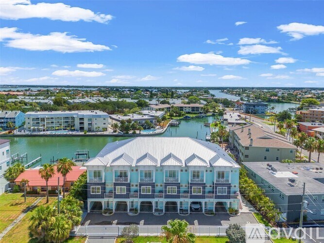A large building with a blue and white facade is the focal point of a residential area with a body of water in the background.