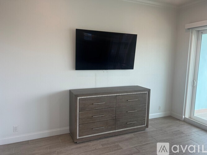 A black TV is mounted on a white wall above a wooden cabinet with drawers.