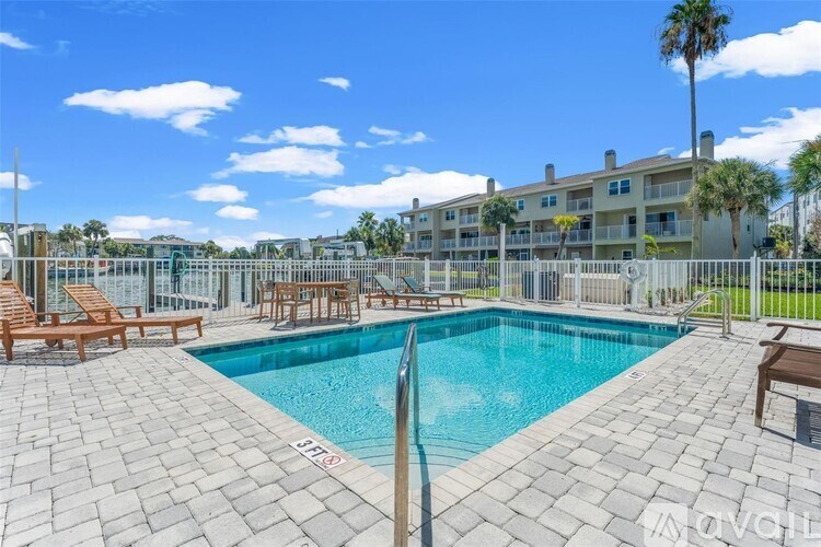 A pool surrounded by a patio and chairs with a building in the background.