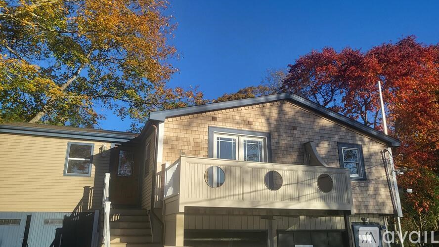 A house with a balcony and a window is surrounded by trees with autumn leaves.