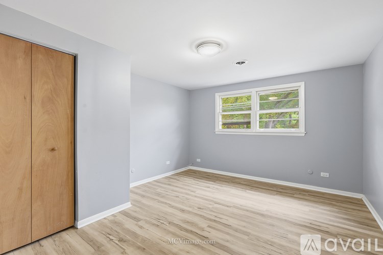 A room with a wooden floor and a window showing trees outside.