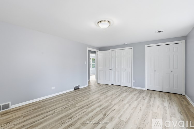 A room with wooden flooring and white walls, featuring a ceiling light and two white doors.