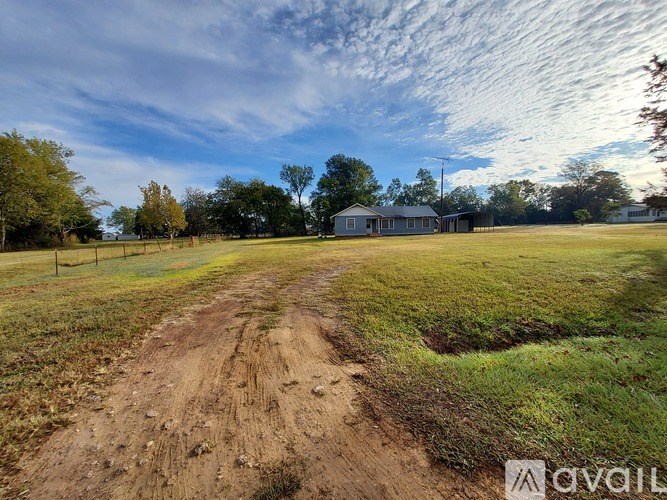 A dirt path leads to a small building in a grassy field.