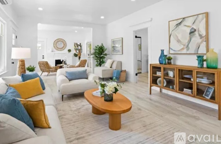 A living room with a white couch, a wooden coffee table, and a white wall with a painting on it.