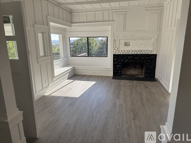 A room with a fireplace and a window overlooking a tree.