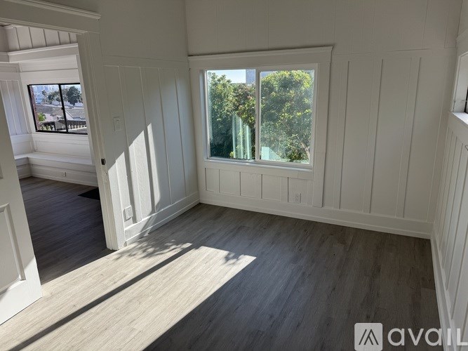 A room with white walls and a window overlooking a green area.