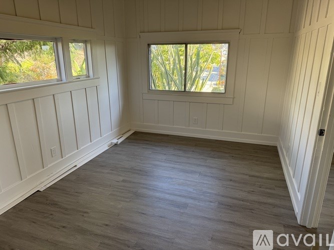 A room with wooden floors and white walls with two windows.