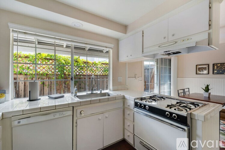 A kitchen with white appliances and a window with plants on the other side.