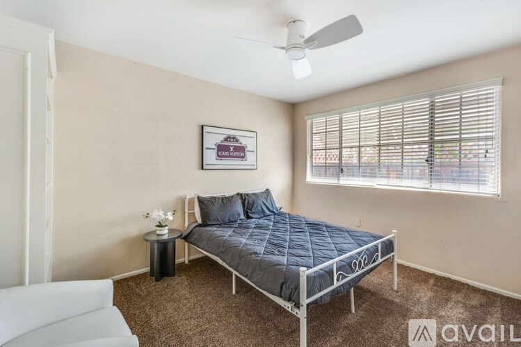 A bedroom with a bed, a small table, and a window with blinds.
