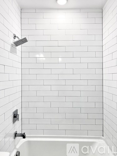 A white tiled shower with a white tub and a white shower head.