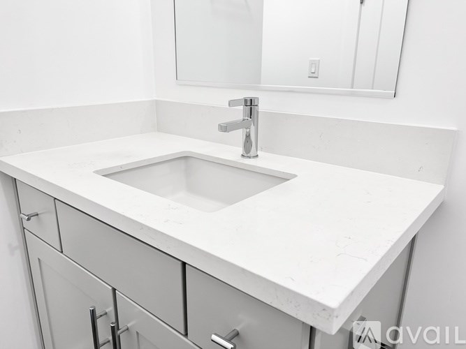 A white sink is in a white countertop with a white cabinet and a white wall.