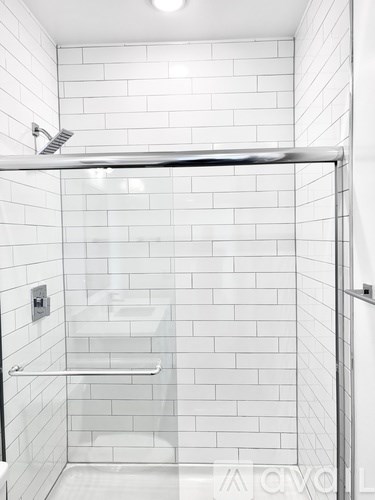 A white tiled shower with a glass door and a metal railing.