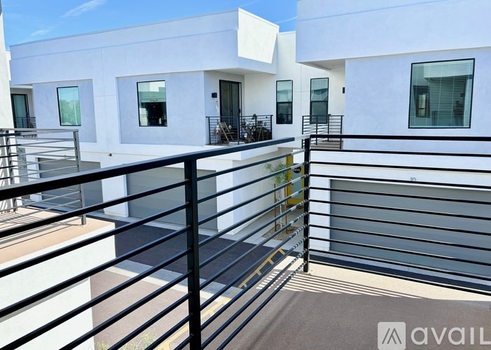 A balcony with a black railing and a white building in the background.