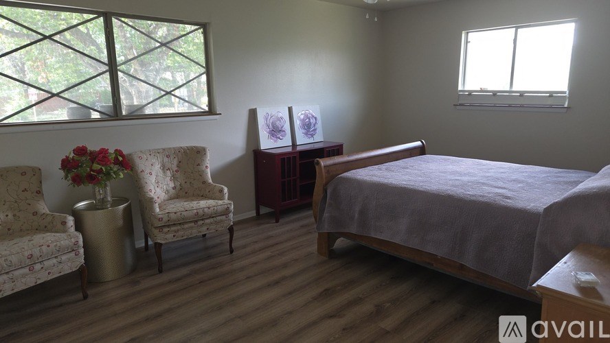 A bedroom with a bed, two chairs, and a table with flowers.