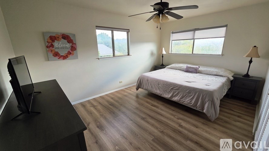 A bedroom with a bed, two chairs, and a ceiling fan.