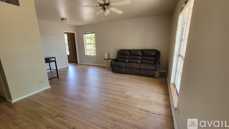 A living room with a black leather couch and wooden flooring.