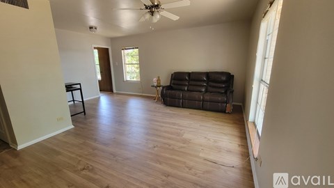 A living room with a black leather couch and wooden flooring.