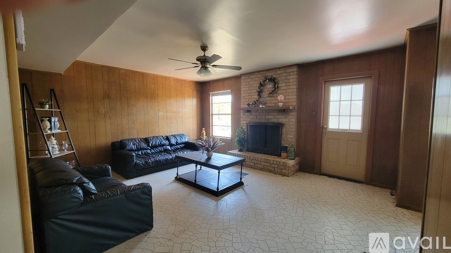 A living room with a black couch, a fireplace, and a ceiling fan.