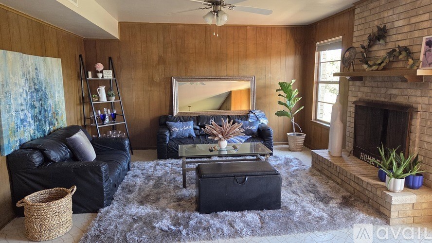 A living room with a black leather couch and wooden flooring.