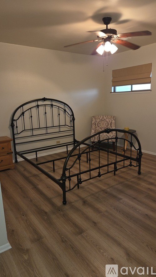 A black metal bed frame in a room with wooden flooring and a ceiling fan.