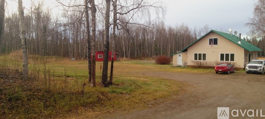 A house with a green roof is surrounded by trees and has a dirt road leading to it.