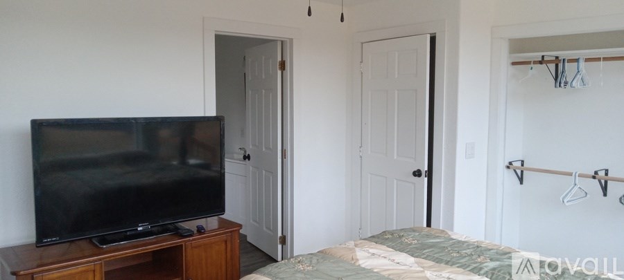 A black TV sits on a wooden stand in a room with a bed and a closet.