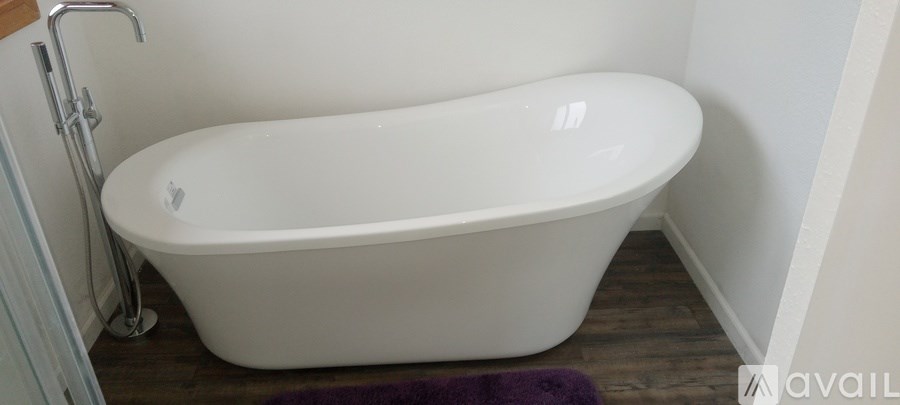 A white bathtub is in a bathroom with a purple rug.