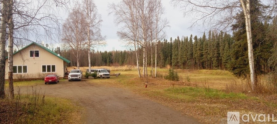 A house with a green roof is surrounded by trees and a dirt road.