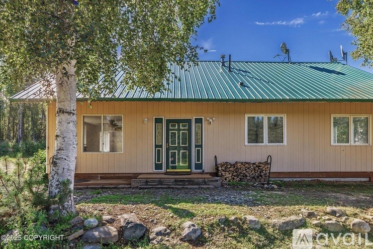 A house with a green roof and a wooden exterior is surrounded by trees.