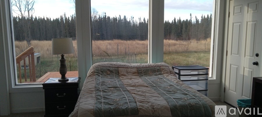 A bedroom with a bed, nightstand and a window overlooking a field.