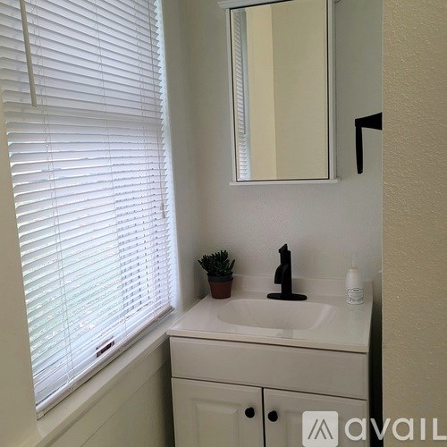 A bathroom with a sink, mirror, and a window with blinds.