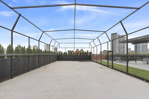 A large, empty, black-framed enclosure with a concrete floor and a view of a city skyline in the distance.