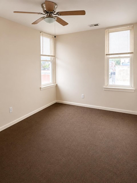A room with a ceiling fan and two windows.