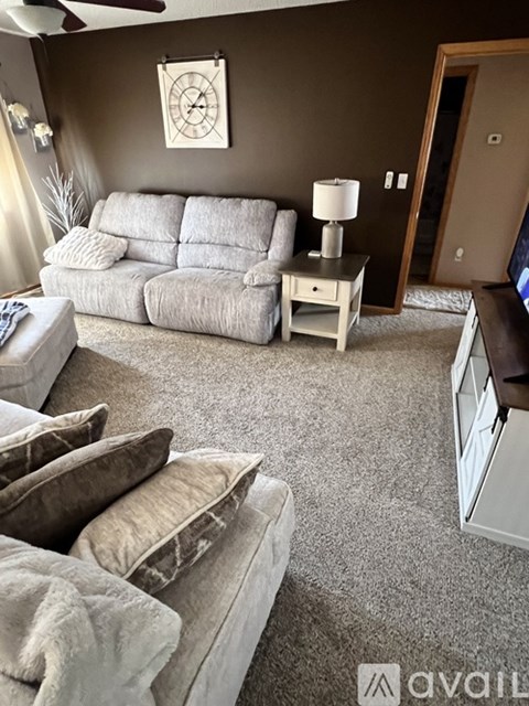 A living room with a grey sofa and a white side table with a lamp.