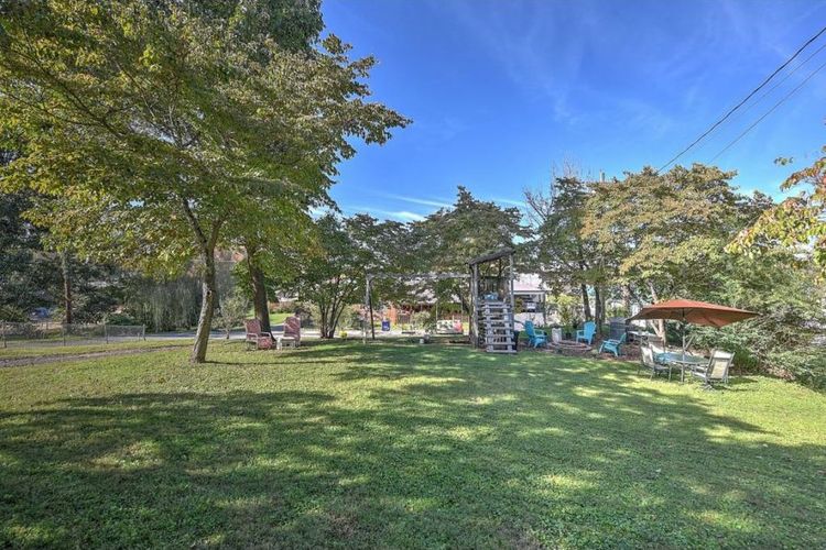 A backyard with a lawn, trees, and a swing set.