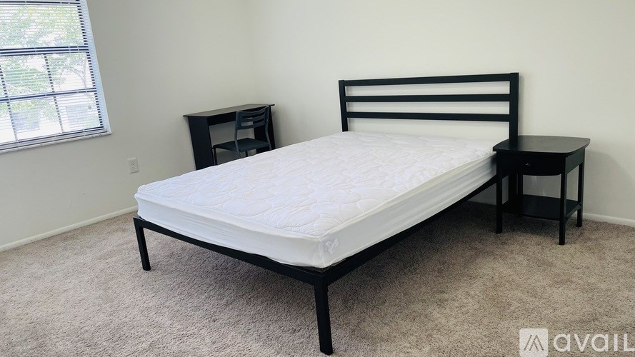 A bed with a white mattress and a black headboard is in a room with a carpeted floor.