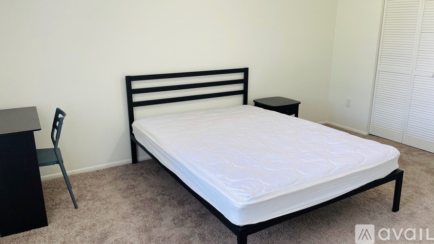 A bed with a white mattress and a black frame is in a room with a carpeted floor.