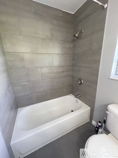A white bathtub sits in a bathroom with grey tiled walls.