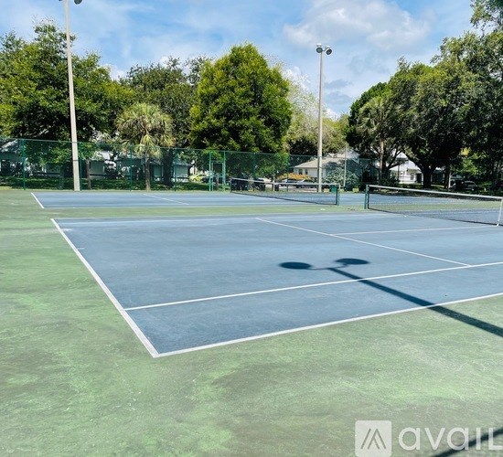 A tennis court surrounded by a green fence and trees.