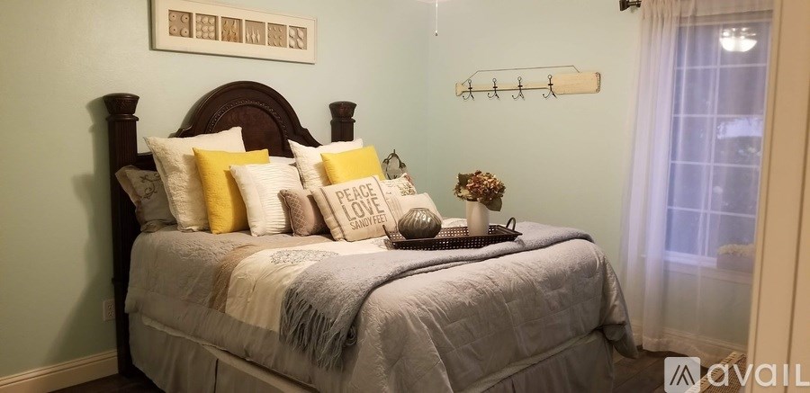 A bed with a grey comforter and pillows with the word "peace" on them.