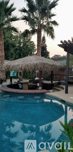 A pool with a thatched roof and palm trees in the background.